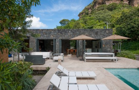 A modern outdoor living space with a stone wall, covered seating areas, and a pool.