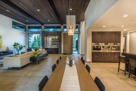 Expansive open floor plan with wood-paneled ceilings, floor-to-ceiling windows, and modern appliances.
