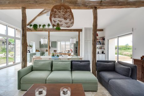 Rustic open-concept living room with wooden beams, hanging lamp, and modern furnishings.