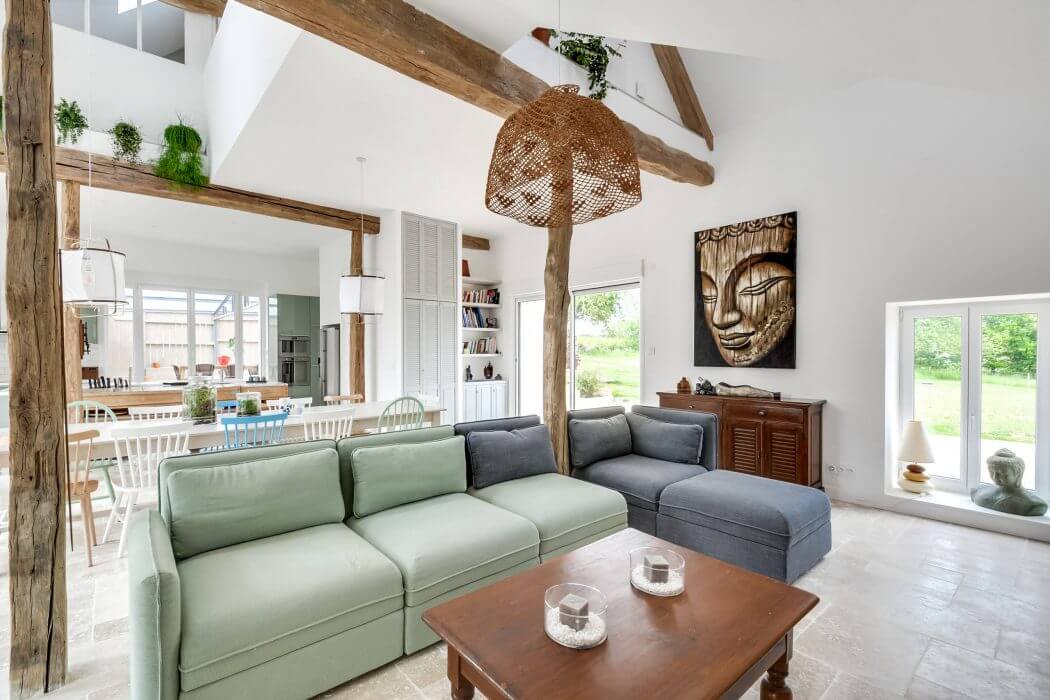 Rustic open-concept living space with exposed beams, green sofa, and Buddha artwork.