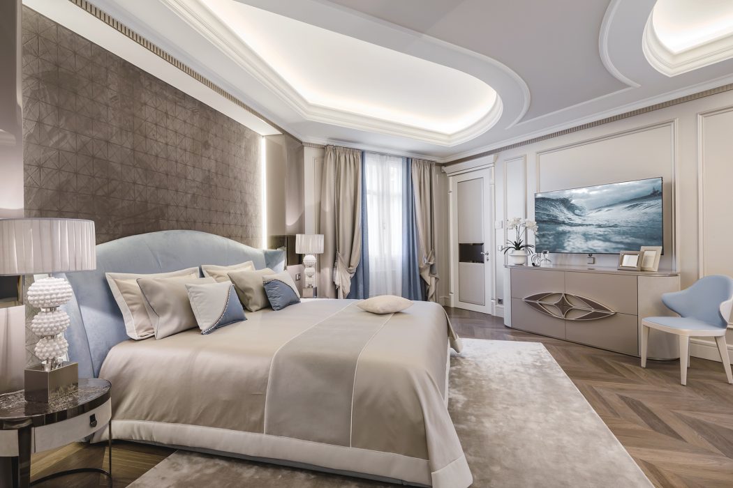 Luxurious bedroom with intricate ceiling molding, plush bedding, and modern furnishings.
