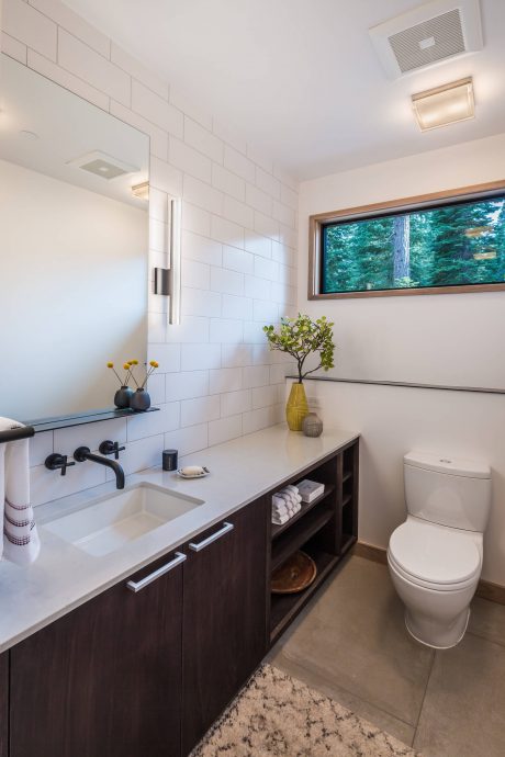 Well-designed bathroom with white tiles, dark wood vanity, and large window offering green views.