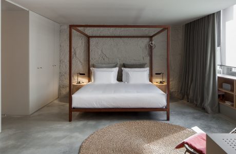 Spacious bedroom with stark concrete walls, wooden four-poster bed, and round woven rug.