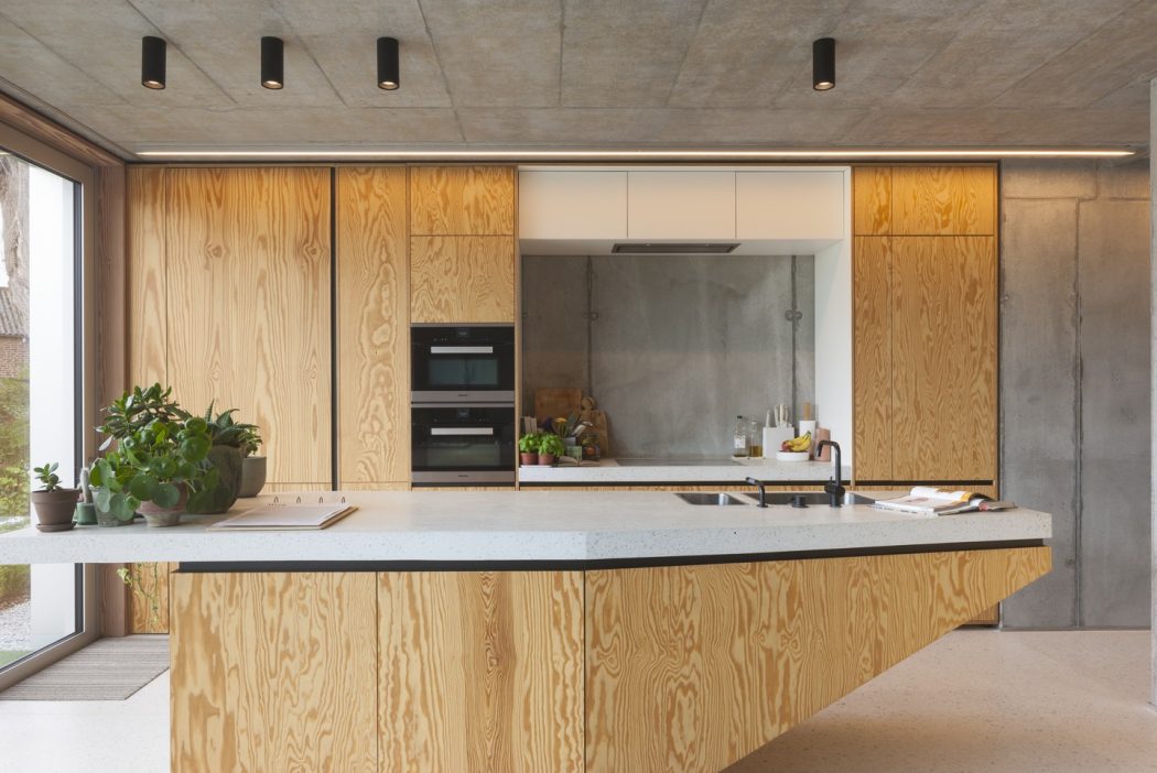 A modern kitchen with an exposed concrete ceiling, wooden cabinetry, and a central island.