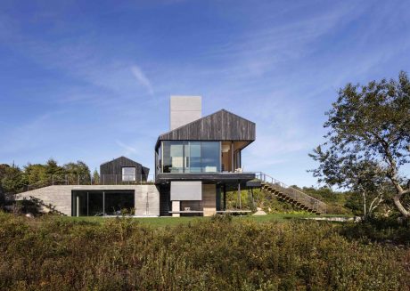 Striking contemporary home with clean lines, wood cladding, and elevated deck against a lush landscape.