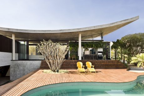 A modern outdoor patio with a curved concrete roof, a wooden deck, and a swimming pool.