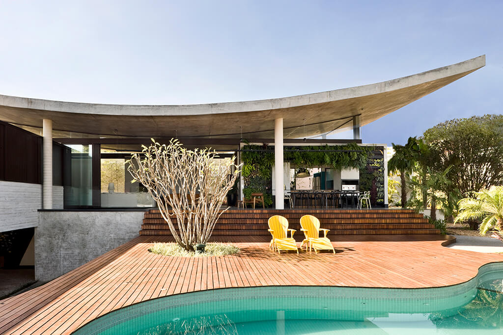 A modern outdoor patio with a curved concrete roof, a wooden deck, and a swimming pool.