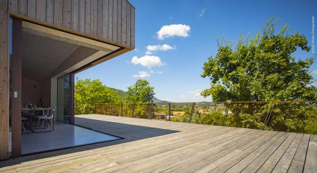 Expansive wooden deck with glass railing overlooking lush green landscape.