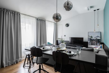 A modern living room with sleek furniture, pendant lights, and a large TV on a black entertainment unit.