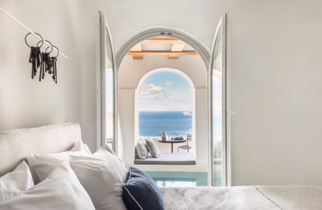 Serene bedroom with arched window frame overlooking tranquil sea view and horizon.
