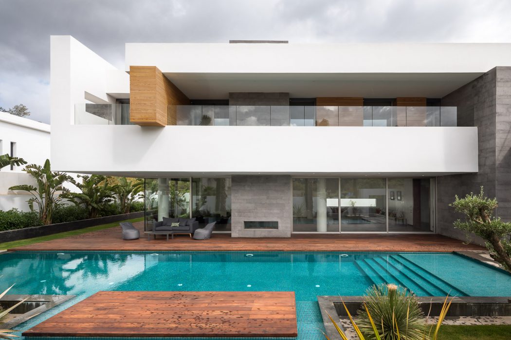 Modern, sleek architecture with a large glass-walled living space, wooden deck, and swimming pool.