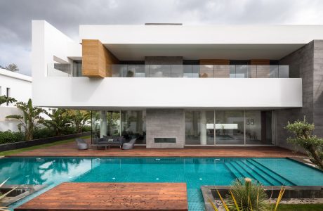 Modern, sleek architecture with a large glass-walled living space, wooden deck, and swimming pool.