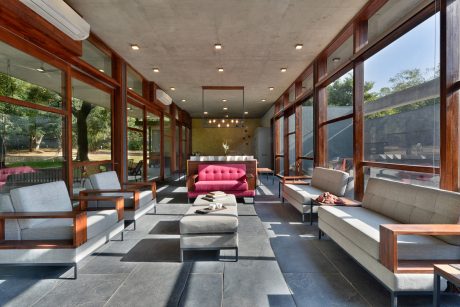 A modern, open-concept living space with wood accents, large windows, and a striking pink sofa.