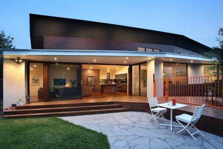 Modern open-plan home with expansive covered patio, wood accents, and stone paving.