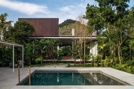 A modern wooden home with a pool and surrounding lush greenery, showcasing seamless indoor-outdoor living.