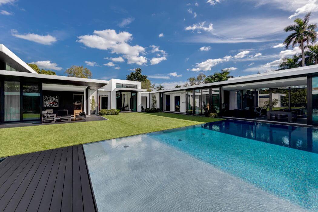 Sleek modern architecture with expansive glass walls, lush landscaping, and a stunning pool.
