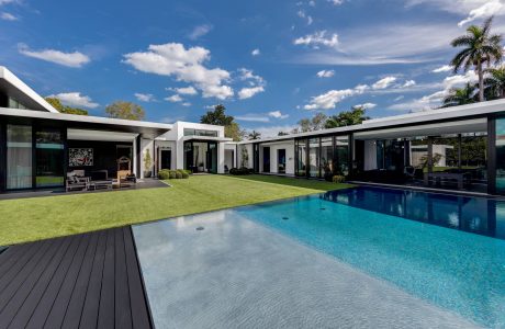 Sleek modern architecture with expansive glass walls, lush landscaping, and a stunning pool.