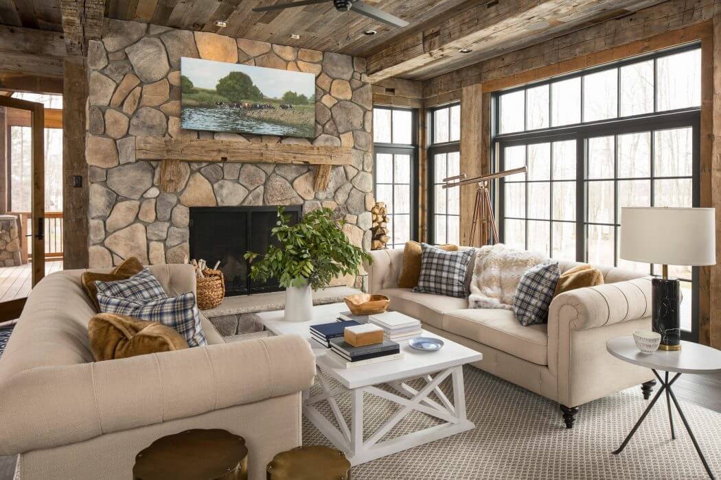 A cozy and rustic living room with exposed stone walls, wooden beams, and large windows.