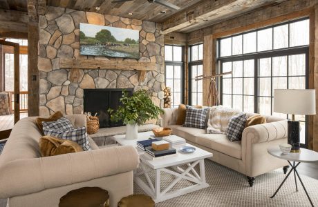 A cozy and rustic living room with exposed stone walls, wooden beams, and large windows.