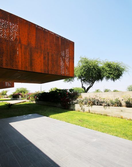 A modern architectural structure with perforated rust-colored panels and lush green landscaping.