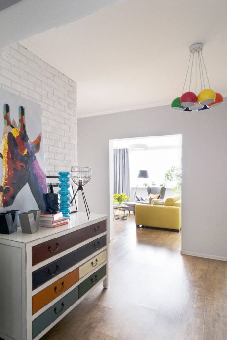 Modern, colorful interior with brick wall, dresser, and view of living room beyond.