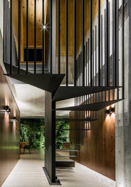 An architectural interior with a striking geometric staircase and wooden walls, bathed in warm lighting.