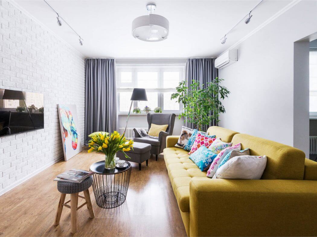 A cozy living room with a vibrant yellow sofa, colorful throw pillows, and a potted plant.