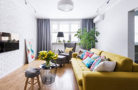 A cozy living room with a vibrant yellow sofa, colorful throw pillows, and a potted plant.