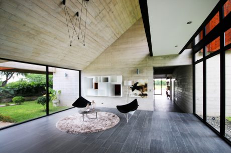 Airy, open-plan interior with vaulted wooden ceiling, sleek furniture, and large windows.