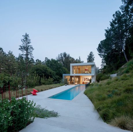 Sleek modern home overlooking a tranquil pool, surrounded by lush greenery.