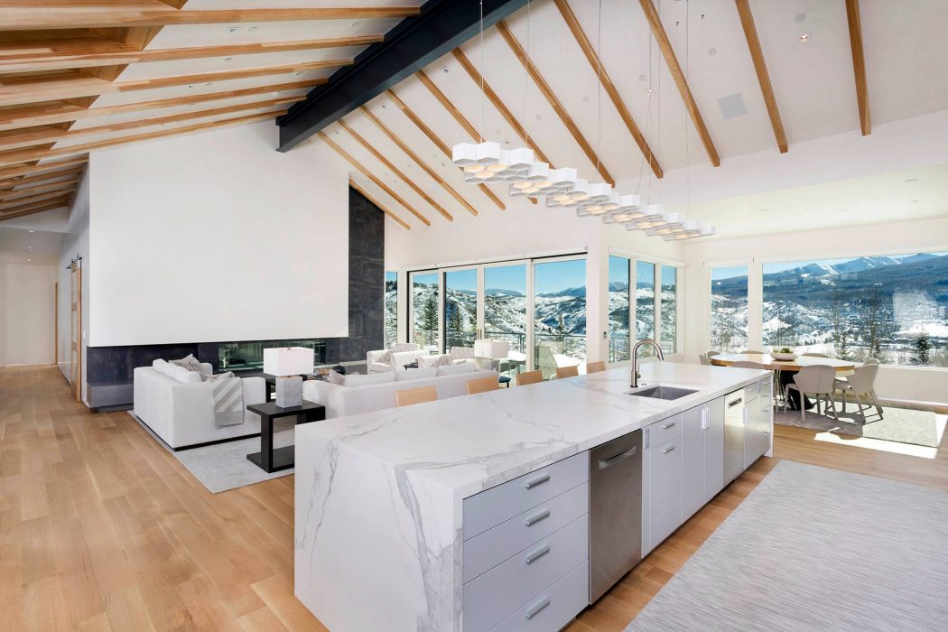 An open-concept living space with a modern kitchen, large windows showcasing mountain views, and an elegant lighting fixture.