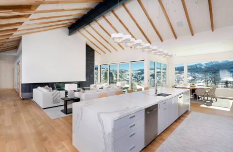 An open-concept living space with a modern kitchen, large windows showcasing mountain views, and an elegant lighting fixture.