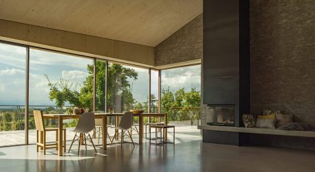 Spacious open-plan living area with large windows, wood furniture, and stone fireplace.