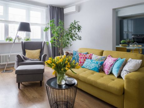 Bright, vibrant living room with a yellow sofa, colorful pillows, and potted plants.