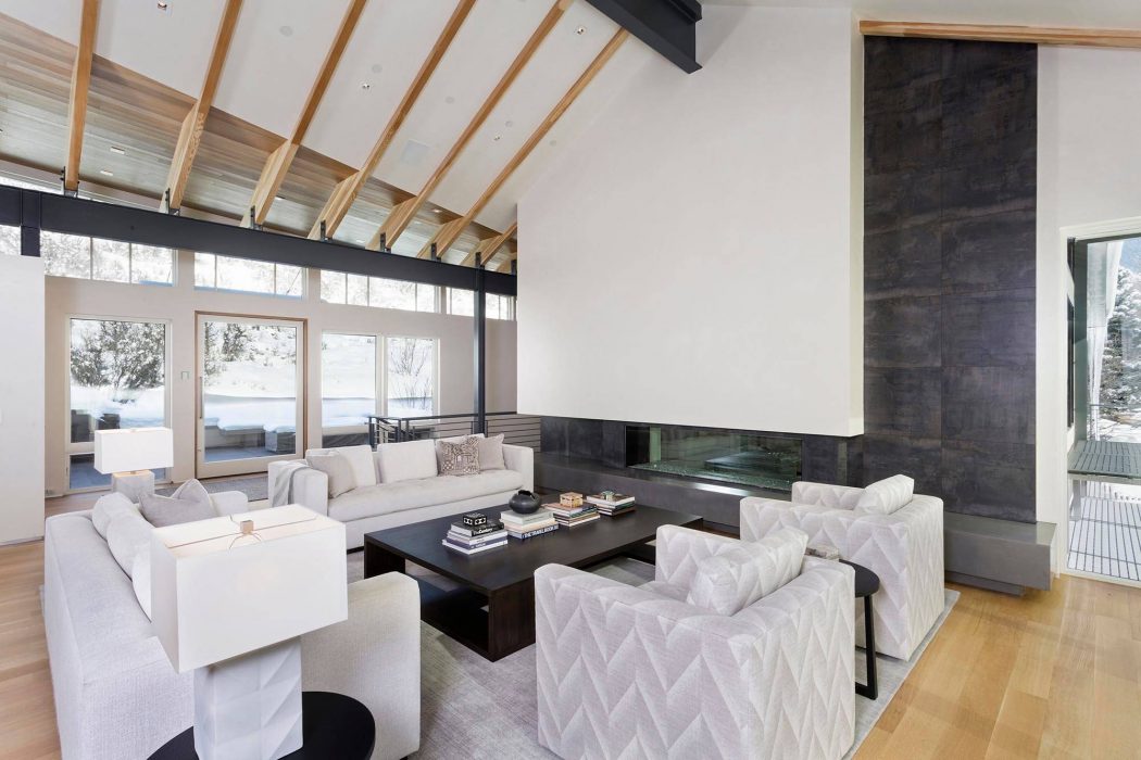 Modern open-concept living room with vaulted ceiling, large windows, and sleek fireplace.