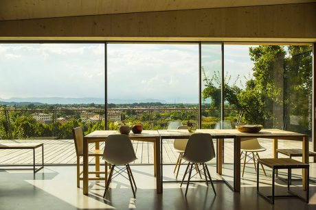 Expansive floor-to-ceiling windows frame a scenic countryside view from an airy dining space.