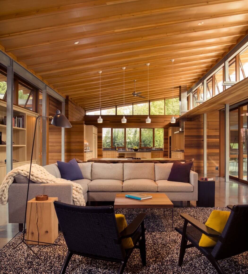 A cozy, rustic living room with a wooden ceiling, large windows, and modern furnishings.