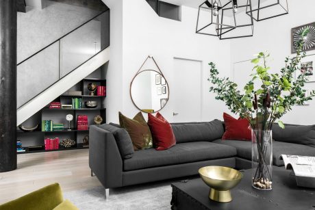 Modern, minimalist living room with bold lighting fixture, sleek gray sofa, and lush greenery.