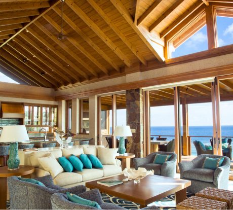 Rustic yet modern living space with high wooden ceilings, large windows, and ocean views.