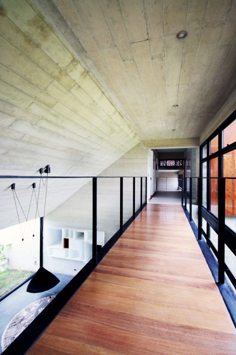 A long, narrow hallway with a wooden floor, exposed concrete ceiling, and metal railings.