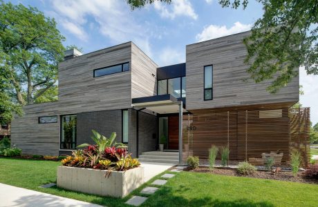 A modern, two-story home with a sleek, wood-paneled exterior and a lush, landscaped garden.