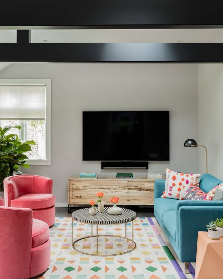 Modern living room with colorful furnishings, geometric patterned rug, and large TV.