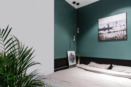 Cozy bedroom with dark green walls, pendant lighting, and nature-inspired artwork.