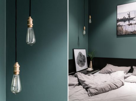 Cozy bedroom with rich green walls, pendant lamps, and a framed artwork on the wall.
