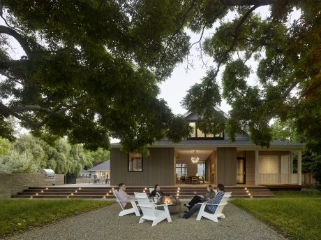 A rustic, modern home with a large porch and steps leading to a firepit gathering area.