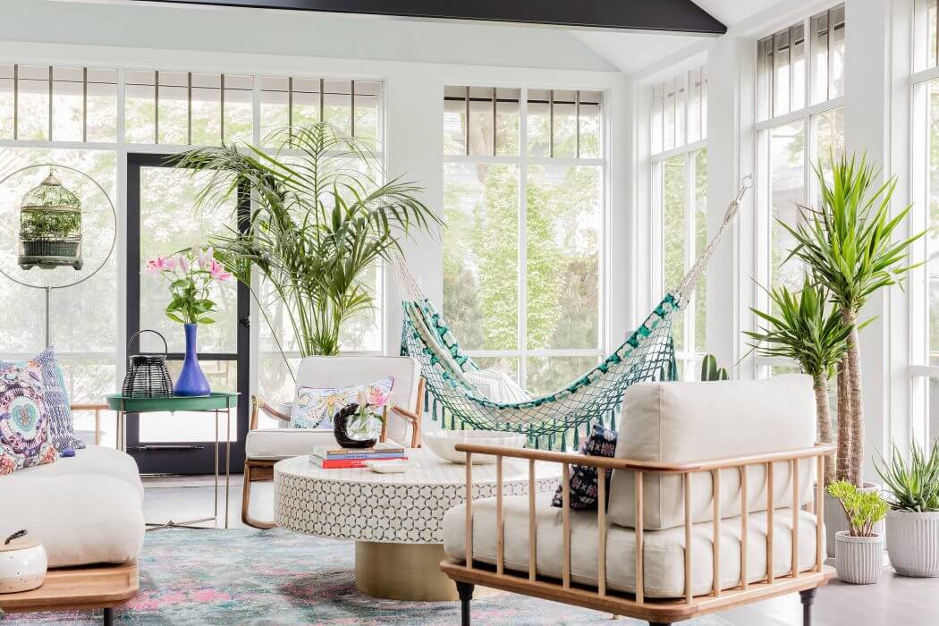 Bright, airy sunroom showcases modern furniture, lush greenery, and open windows.