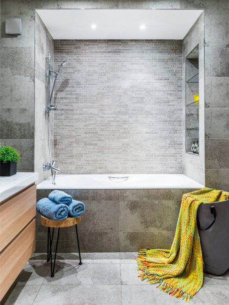 Spacious bathroom with gray brick walls, wood vanity, and vibrant yellow towel.
