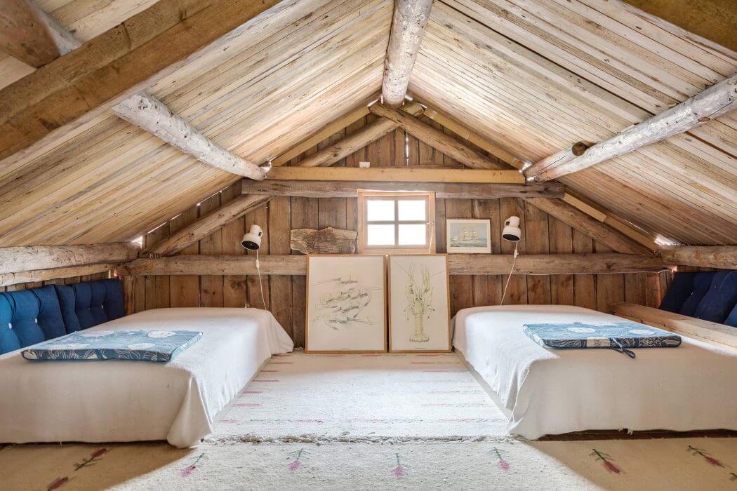 A cozy wooden attic bedroom with an inviting geometric roof, artwork, and plush beds.