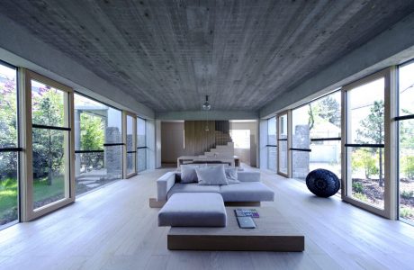 Expansive, minimalist living room with concrete ceiling, large windows, and modern furnishings.