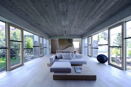 Expansive, minimalist living room with concrete ceiling, large windows, and modern furnishings.